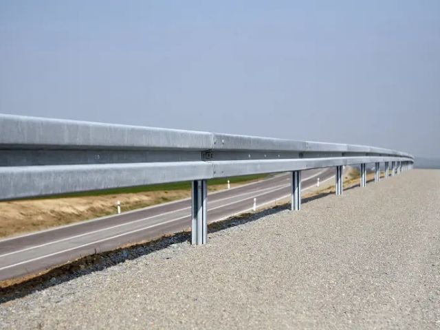 W-Beam Steel Crash Barrier Galvanized steel W-beam crash barrier installed on the side of a road to enhance vehicle safety.